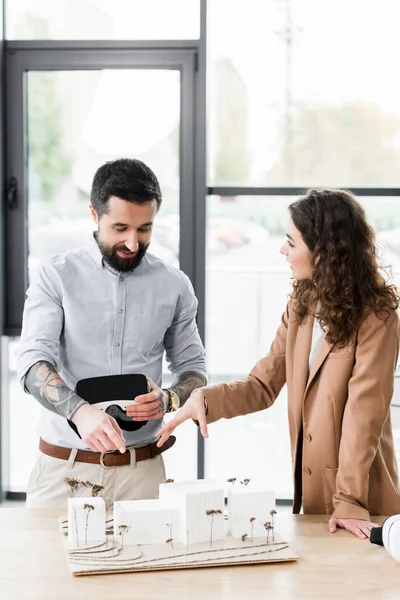 Sorridenti architetti di realtà virtuale che parlano e puntano il dito contro il modello di casa — Stock Photo