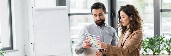 Panoramic shot of smiling virtual reality architects looking at layout of colors — Stock Photo