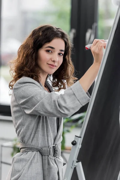 Account manager attraente e sorridente che scrive su flipchart in ufficio — Foto stock