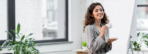 Panoramic shot of smiling and attractive account manager holding cup of coffee — Stock Photo