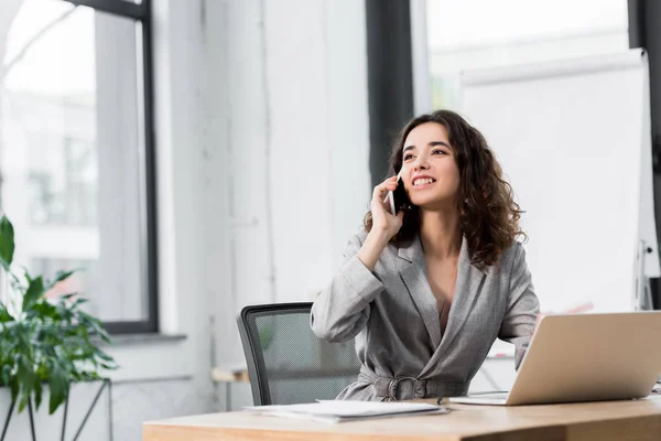 Sorrindo e gerente de conta atraente falando no smartphone no escritório — Fotografia de Stock