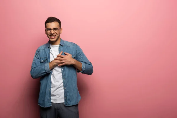 Homme avec les mains sur la poitrine souriant à la caméra sur fond rose — Photo de stock