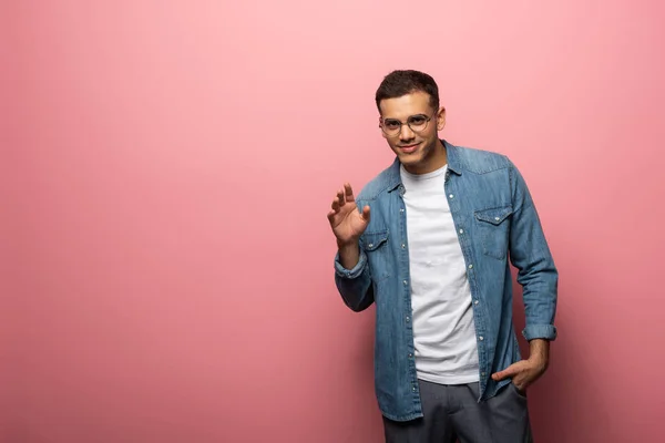 Hombre saludando la mano mientras sonríe a la cámara en el fondo rosa - foto de stock