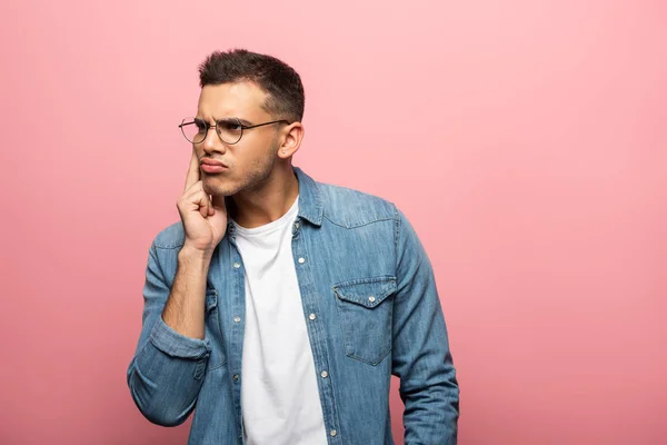 Young thoughtful man with hand by cheek looking away on pink background — Stock Photo