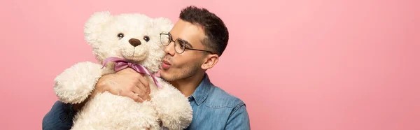 Panoramic shot of young man kissing teddy bear isolated on pink — Stock Photo