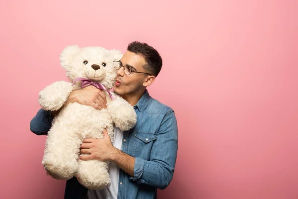 Handsome man kissing teddy bear on pink background with copy space — Stock Photo