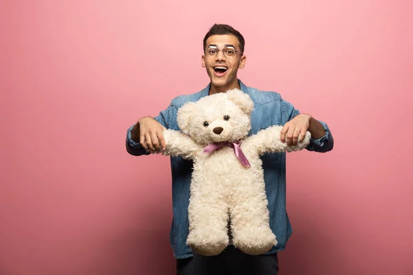 Hombre sorprendido con oso de peluche mirando a la cámara sobre fondo rosa - foto de stock