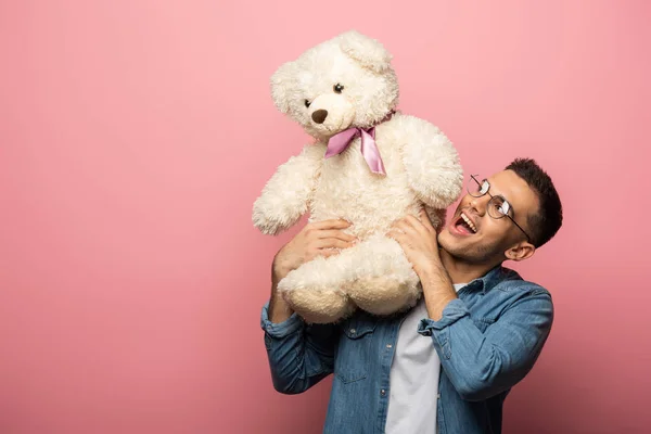 Aufgeregter junger Mann blickt auf Teddybär auf rosa Hintergrund — Stockfoto