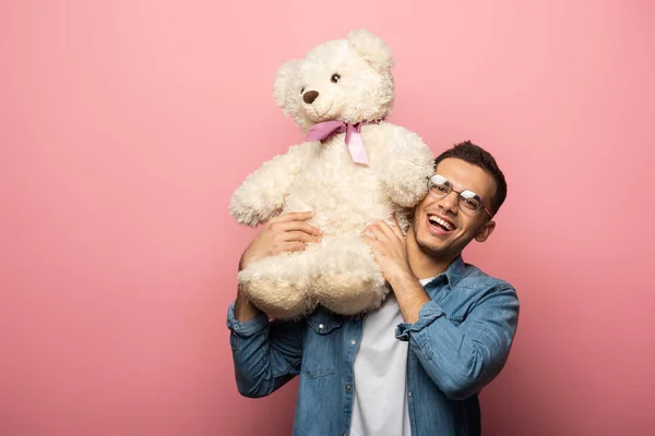Sonriente hombre sosteniendo oso de peluche y mirando a la cámara sobre fondo rosa - foto de stock