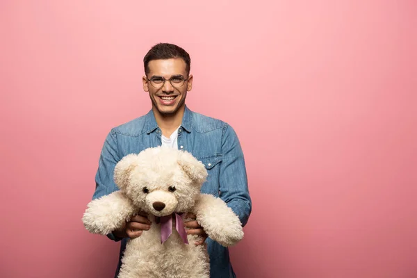 Positive man holding teddy bear and smiling at camera on pink background — Stock Photo