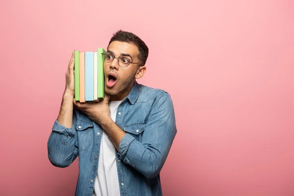 Aufgeregter junger Mann mit bunten Büchern auf rosa Hintergrund — Stockfoto