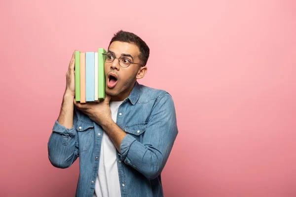 Excited young man holding colorful books on pink background — Stock Photo
