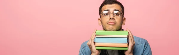 Scatto panoramico di uomo confuso con libri che guardano la macchina fotografica isolata su rosa — Foto stock