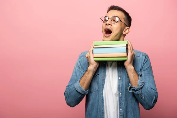 Hombre excitado con libros coloridos mirando hacia otro lado sobre fondo rosa - foto de stock
