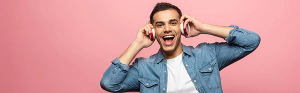 Panoramic shot of cheerful man in headphones looking at camera isolated on pink — Stock Photo