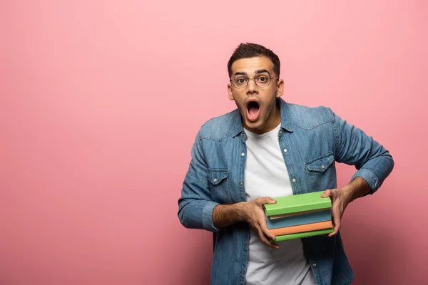 Uomo scioccato in possesso di libri e guardando la fotocamera su sfondo rosa — Foto stock