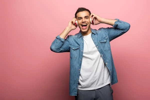 Junger positiver Mann mit Kopfhörer blickt in die Kamera auf rosa Hintergrund — Stockfoto