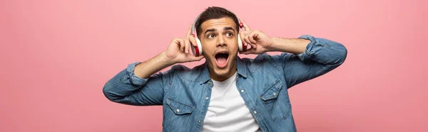 Panoramaaufnahme eines aufgeregten Mannes mit Kopfhörern, der isoliert auf rosa Musik hört — Stockfoto