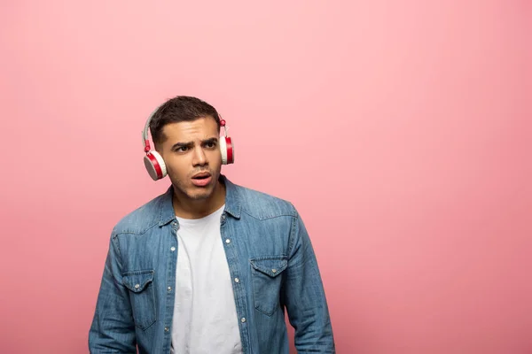 Jeune homme réfléchi dans les écouteurs regardant loin sur fond rose — Photo de stock