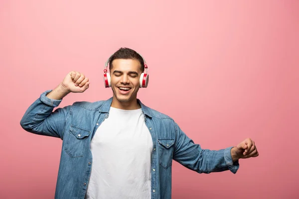 Smiling man with closed eyes dancing while using headphones isolated on pink — Stock Photo