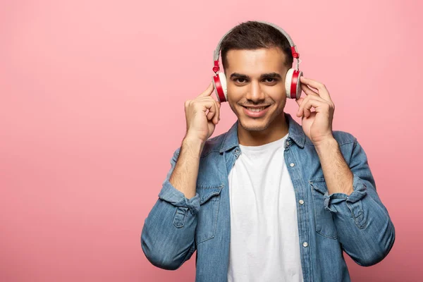 Hombre guapo en auriculares sonriendo a la cámara sobre fondo rosa - foto de stock