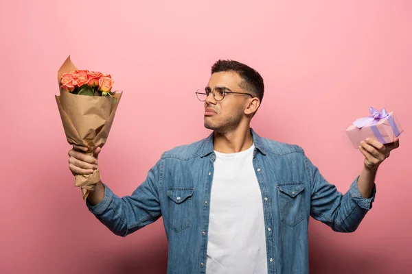 Uomo premuroso in possesso di fiori e presenti su sfondo rosa — Foto stock