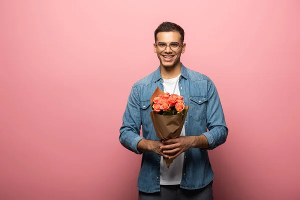 Hombre guapo sonriendo a la cámara mientras sostiene ramo sobre fondo rosa - foto de stock