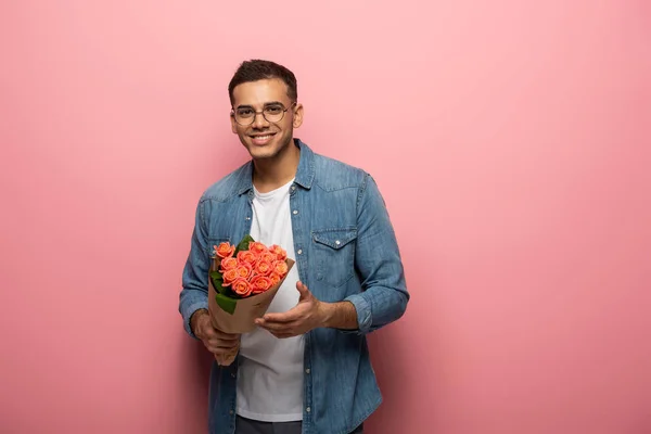 Молодий чоловік з трояндовими квітами посміхається на камеру на рожевому фоні — стокове фото