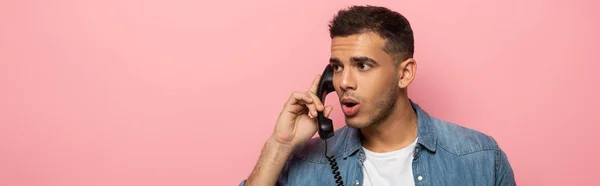 Foto panorámica del hombre sorprendido con auricular telefónico mirando hacia otro lado aislado en rosa - foto de stock