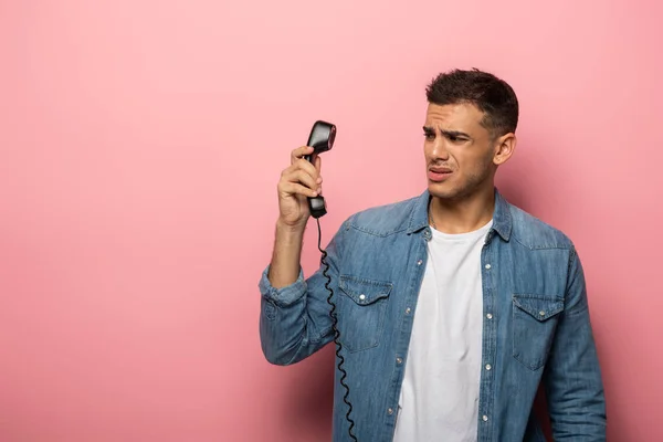 Verängstigter Mann blickt auf Telefonhörer auf rosa Hintergrund — Stockfoto