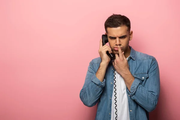 Продуманий чоловік з пальцем за ротом розмовляє по телефону на рожевому фоні — Stock Photo