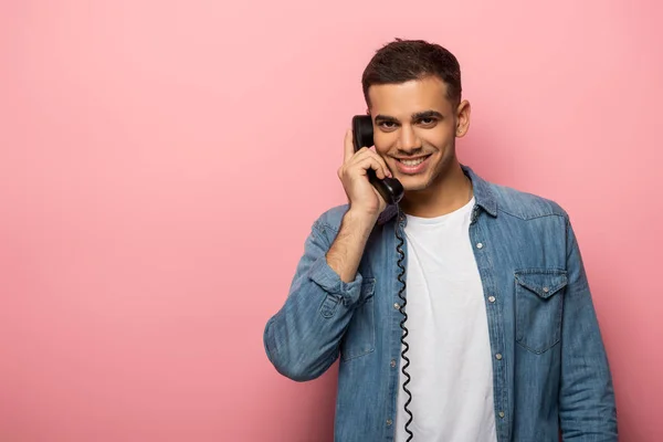 Hombre guapo hablando por teléfono y sonriendo a la cámara sobre fondo rosa - foto de stock