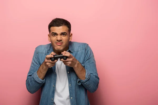 KYIV, UKRAINE - NOVEMBER 12, 2019: Young man with joystick grimacing on pink background — Stock Photo