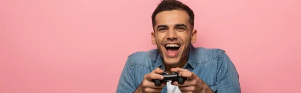 QUIIV, UCRÂNIA - NOVEMBRO 12, 2019: Homem alegre segurando joystick isolado em rosa, tiro panorâmico — Fotografia de Stock