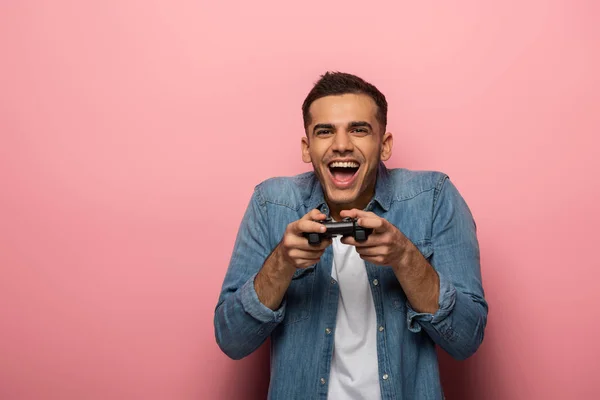KYIV, UKRAINE - NOVEMBER 12, 2019: Excited man holding joystick on pink background with copy space — Stock Photo