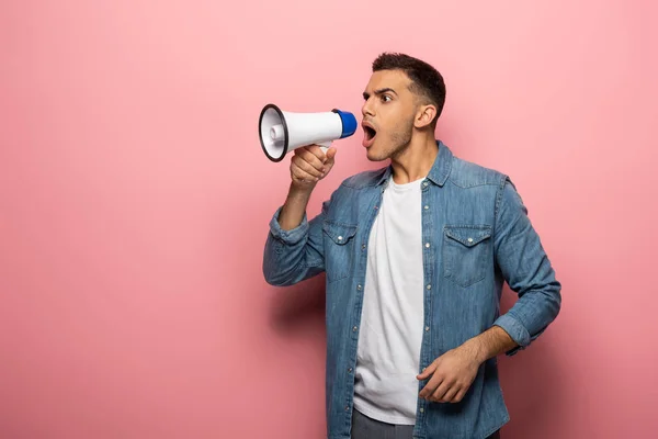 Seitenansicht eines jungen Mannes, der in Lautsprecher auf rosa Hintergrund schreit — Stockfoto