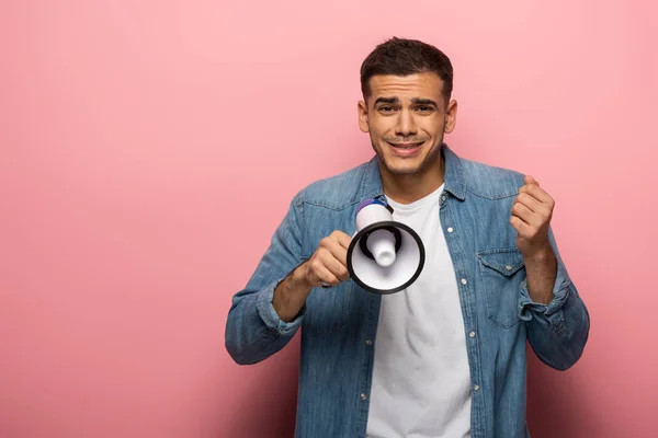 Upset man looking at camera while holding loudspeaker on pink background — Stock Photo