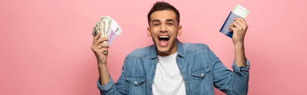 Photo panoramique d'un homme excité tenant de l'argent comptant, un passeport et une carte d'embarquement sur fond rose — Photo de stock