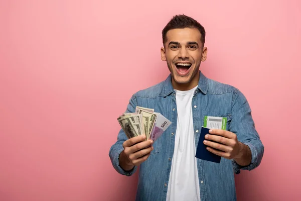 Hombre sorprendido sosteniendo moneda, tarjeta de embarque y pasaporte sobre fondo rosa - foto de stock