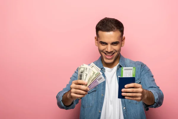 Homme tenant un passeport avec carte d'embarquement et de l'argent tout en souriant à la caméra sur fond rose — Photo de stock