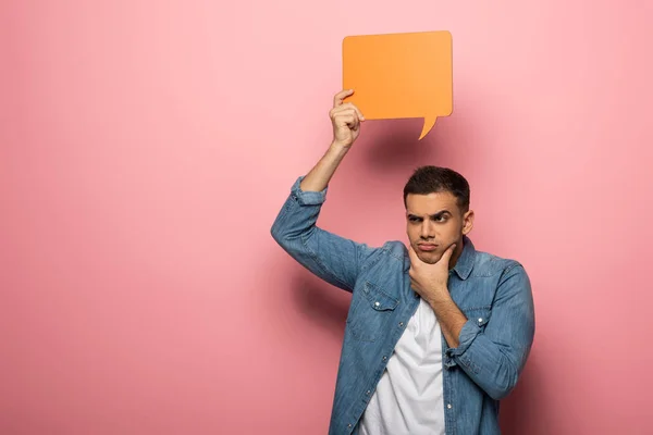 Thoughtful man with hand by chin holding speech bubble on pink background — Stock Photo