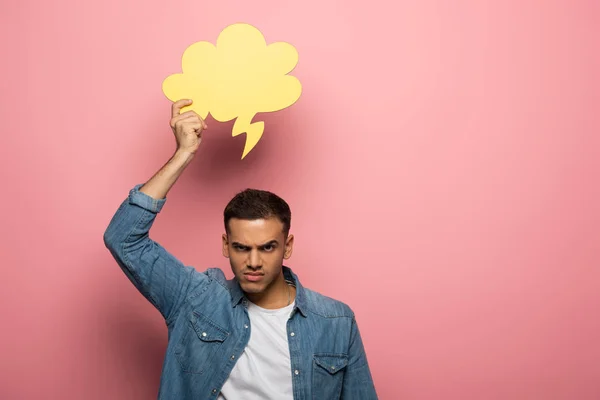 Angry man looking at camera while holding speech bubble on pink background — Stock Photo