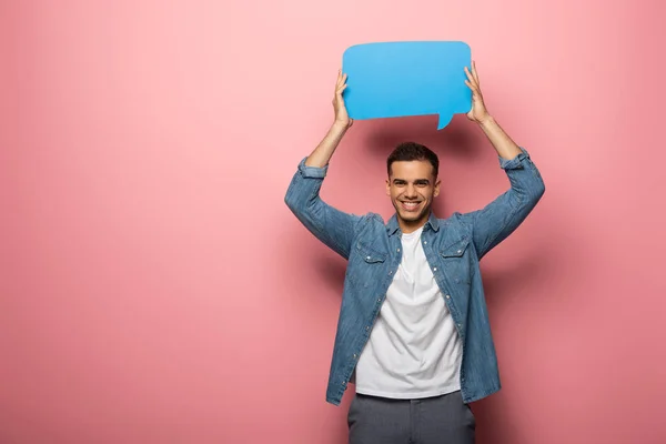 Sorridente giovane uomo che tiene la bolla discorso e guardando la fotocamera su sfondo rosa — Foto stock