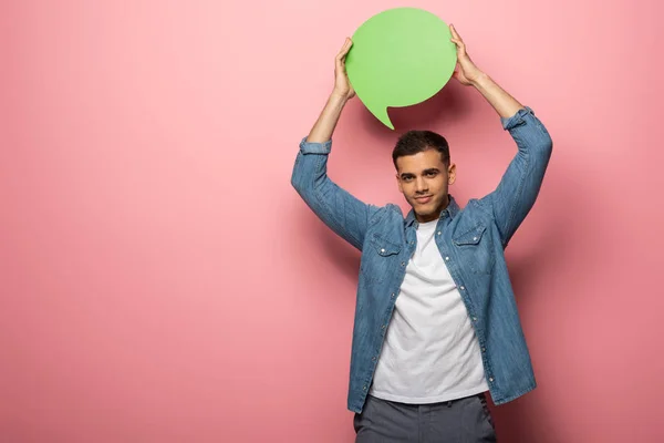 Hombre guapo sosteniendo la burbuja del habla y mirando a la cámara en el fondo rosa - foto de stock