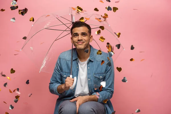 Homme rêveur avec parapluie sous confettis tombants sur fond rose — Photo de stock