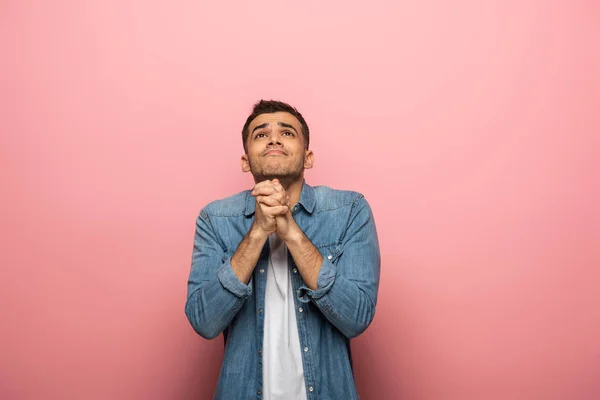 Hombre de ensueño con las manos orando mirando hacia otro lado sobre fondo rosa - foto de stock
