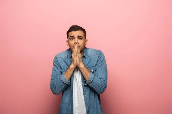 Joven han con gesto de oración mirando a la cámara sobre fondo rosa - foto de stock