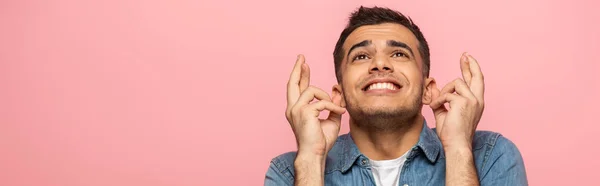 Panoramic shot of smiling man with crossed fingers looking away isolated on pink — Stock Photo