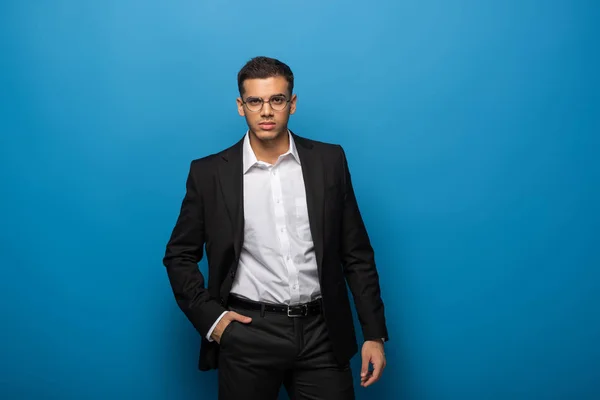 Handsome businessman with hand in pocket looking at camera on blue background — Stock Photo