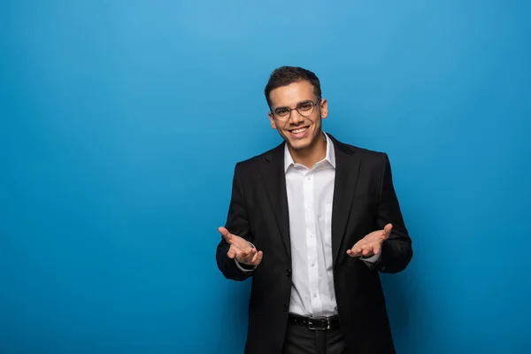 Smiling businessman presenting something and looking at camera on blue background — Stock Photo